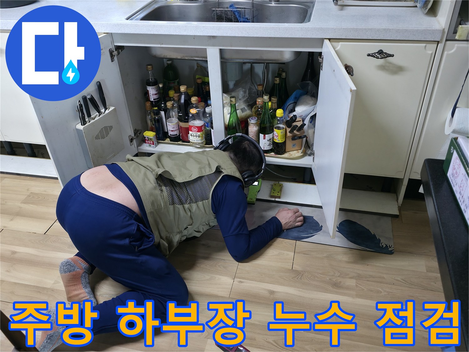 싱크대 아래 좁은 공간에서 배관 상태를 면밀히 관찰하는 작업자
