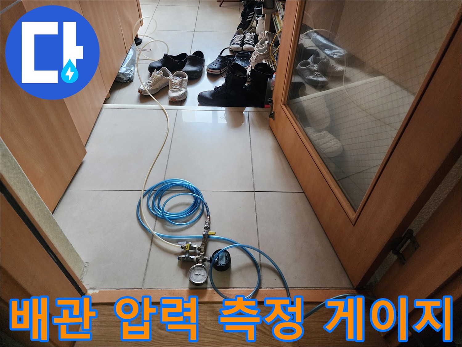 바닥 타일 위에 놓인 파란색 호스와 압력계 장치