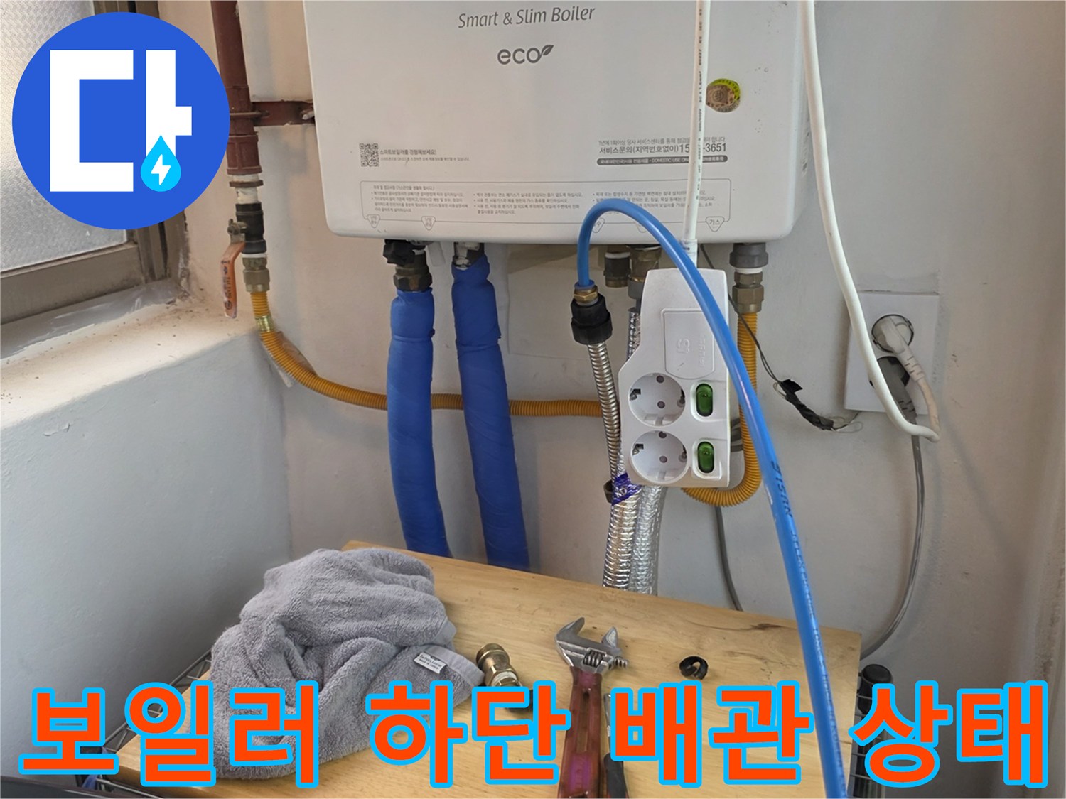 파란색 호스와 전기 콘센트가 있는 보일러 하부 설치 모습