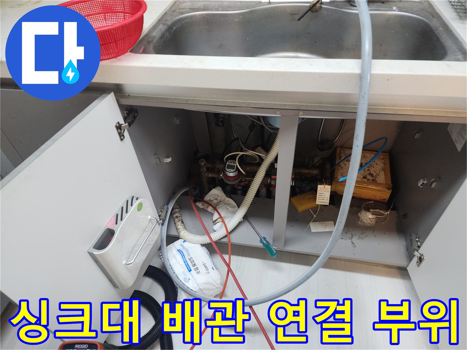 싱크대 하부의 복잡한 배수 호스와 연결된 배관 구조입니다.