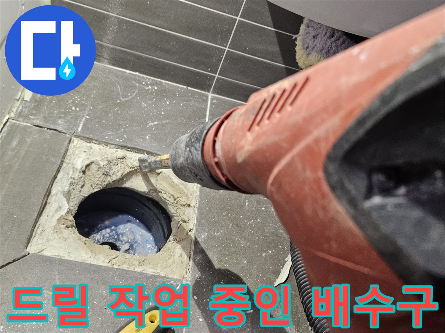 전동 드릴을 사용하여 배수구 주변의 타일을 파쇄하는 장면입니다.