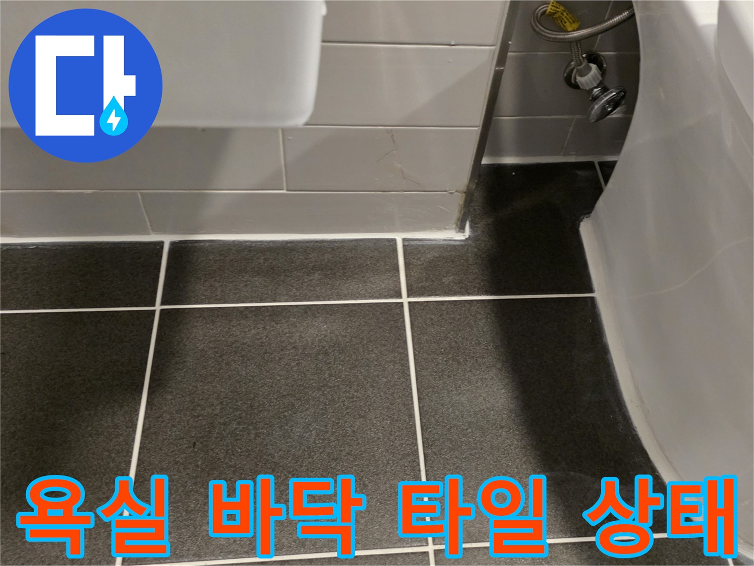 어두운색 욕실 타일과 세면대 아래 배관 모습