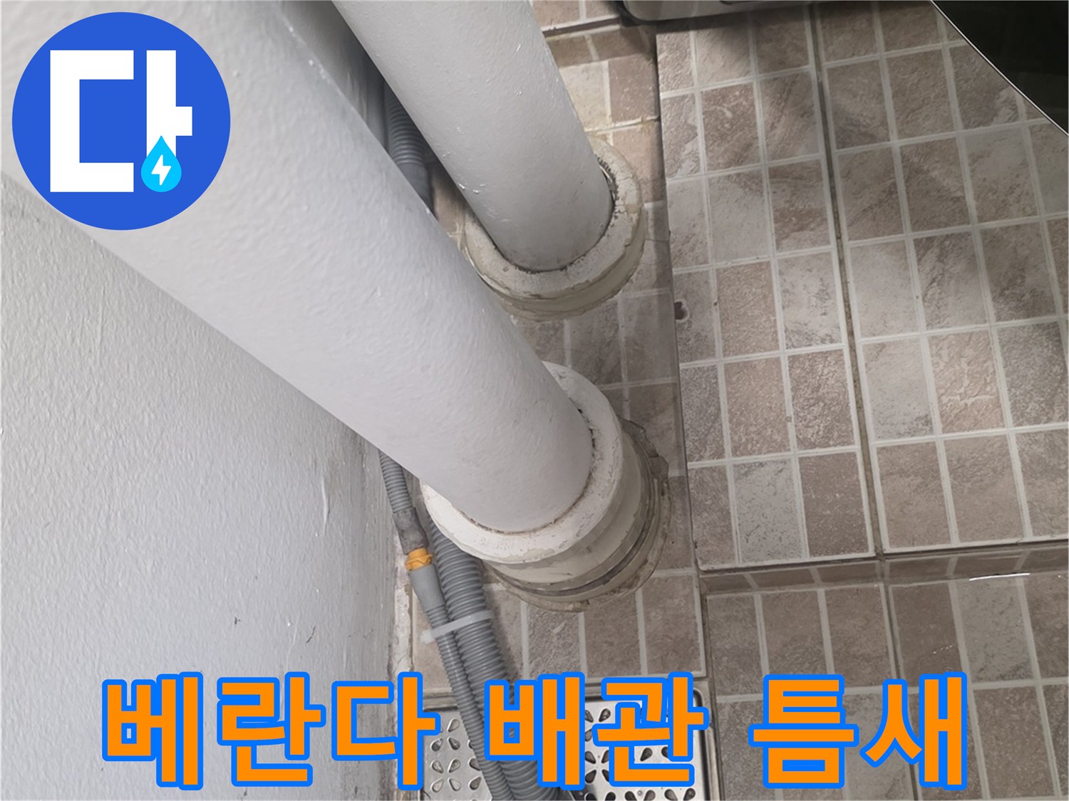 타일 바닥에 노출된 세탁기 배수 호스와 수직 배관 접합부