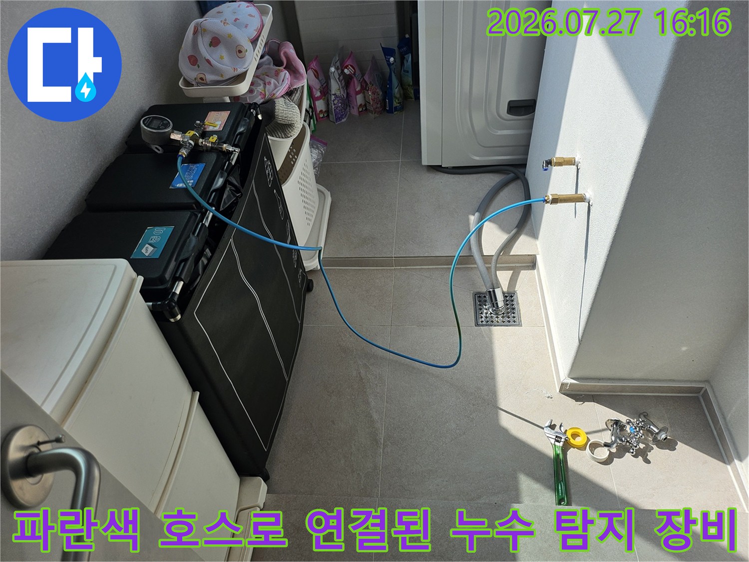검은색 가전제품 옆으로 파란색 호스가 길게 이어져 벽면 배관 밸브에 연결된 모습
