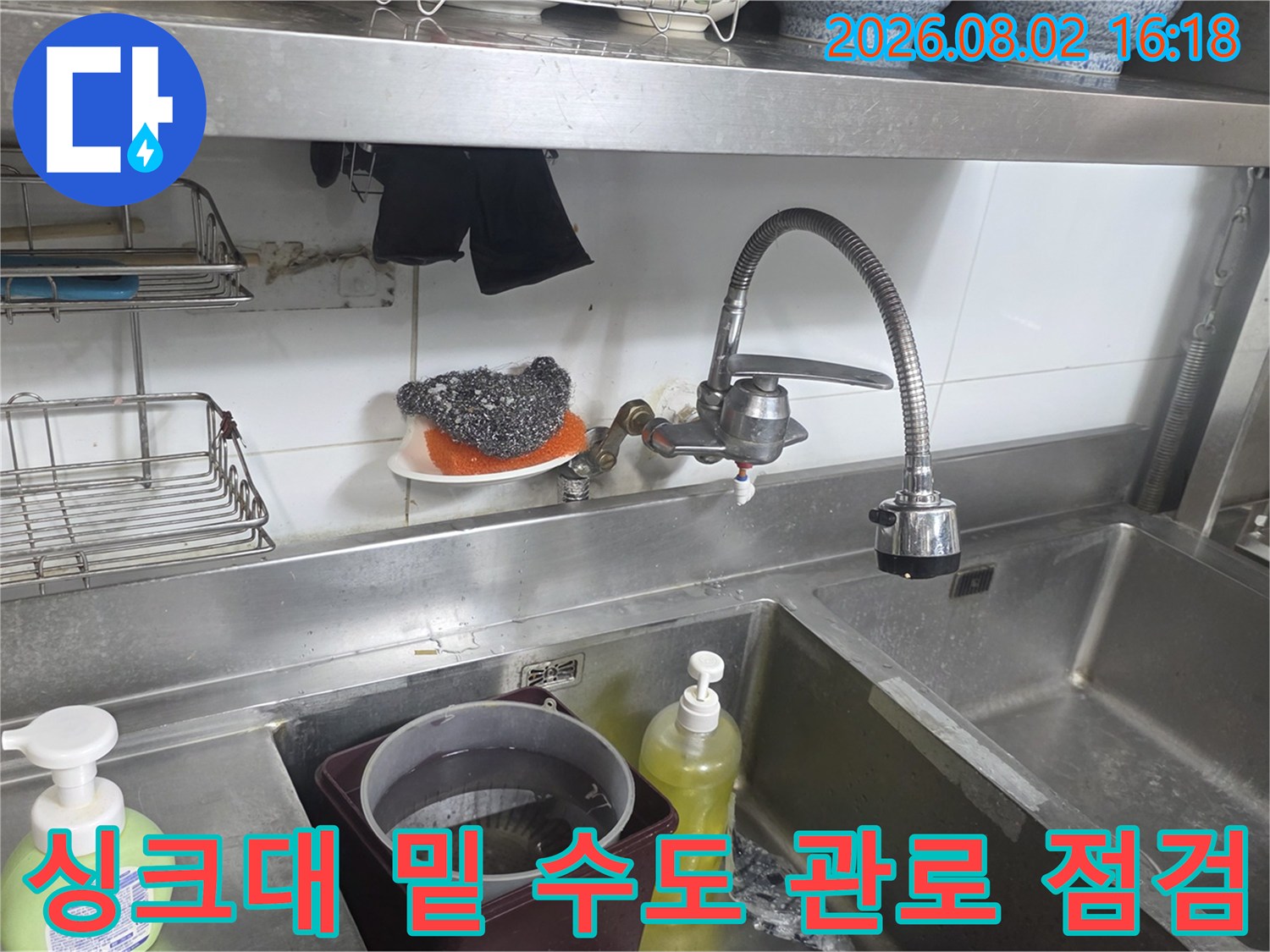 상업용 싱크대 하부의 은색 수전과 물 공급을 위한 배관 시스템