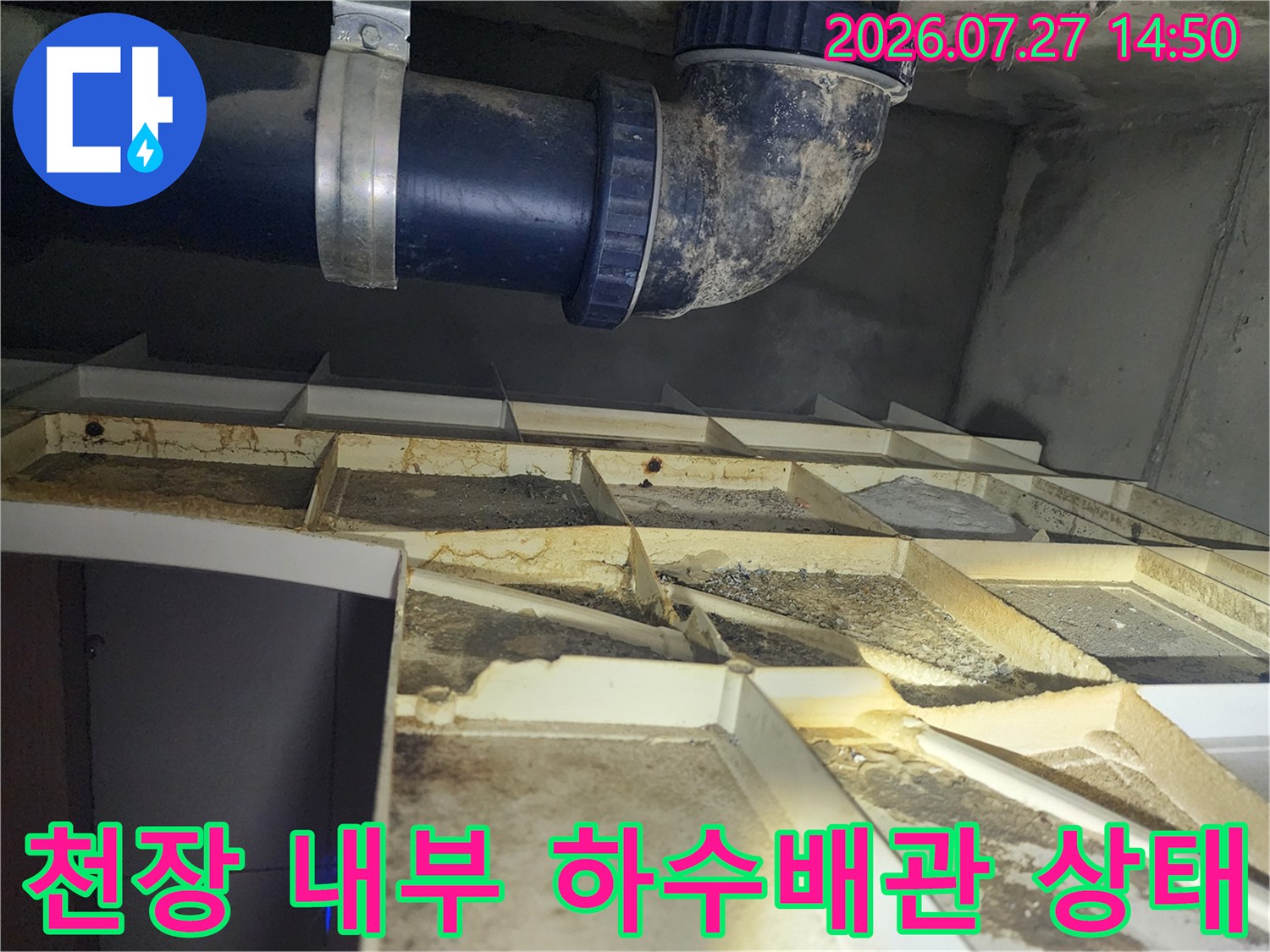 건물 천장 점검구 내부의 파란색 플라스틱 하수 배관과 오염된 천장 구조물