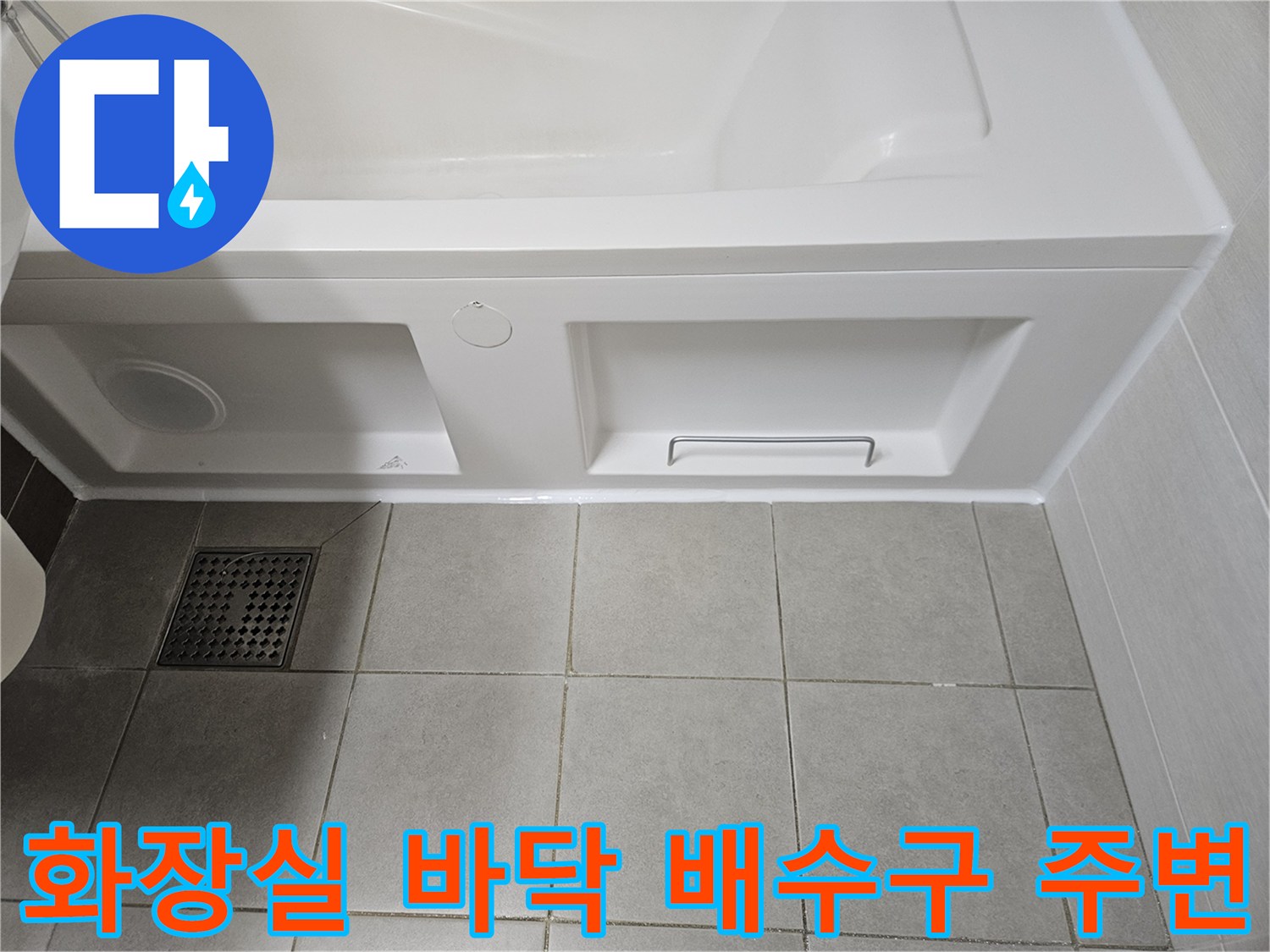 욕실 욕조 패널 하부와 타일 배수구 유가 근접 촬영본입니다.