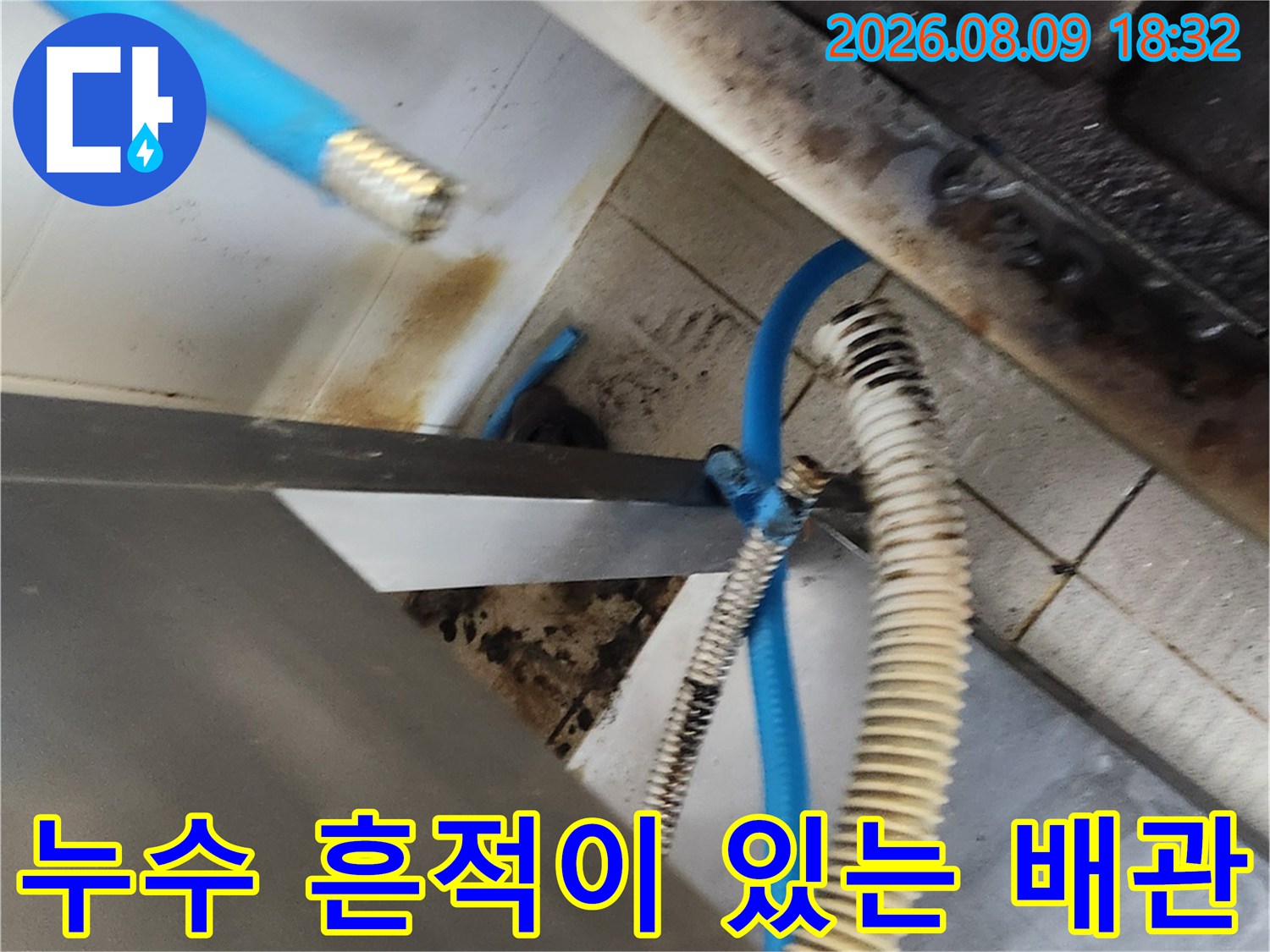 물기가 남아있는 싱크대 하단 금속 부속과 파란색 호스