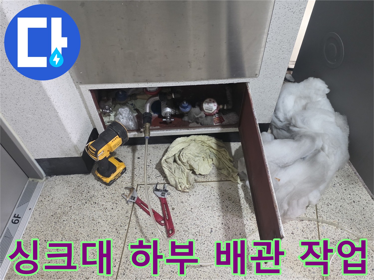 작업자가 사용 중인 전동 드릴과 렌치가 싱크대 아래 배관 주변에 배치된 사진