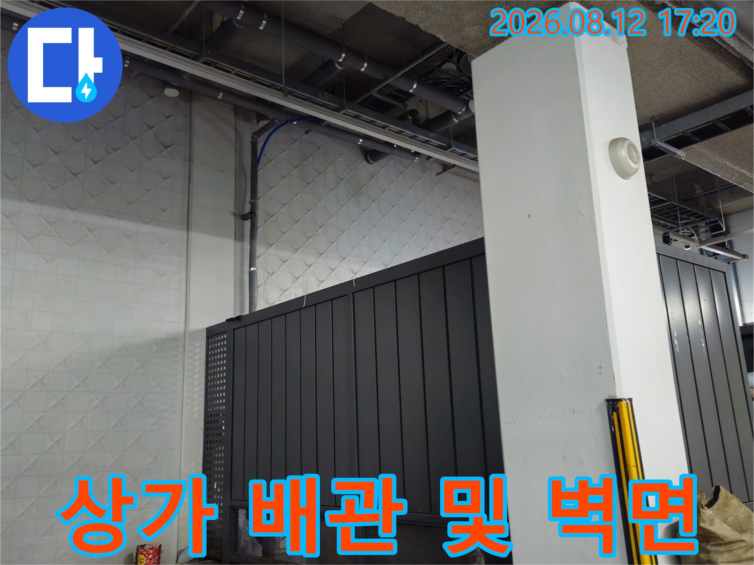 상가 지하 주차장 내 노출된 천장 배관과 타일벽의 모습입니다.