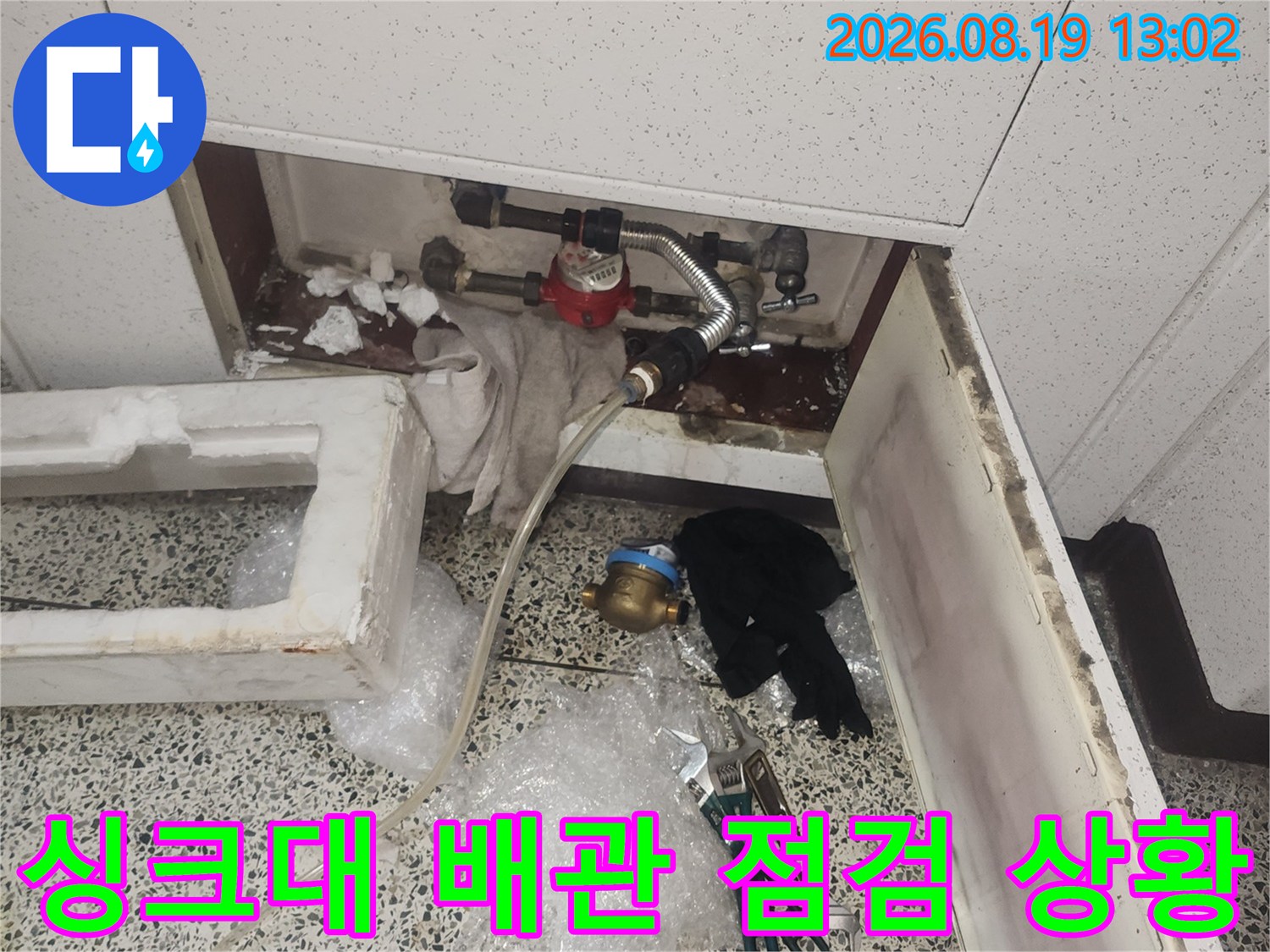 싱크대 하부장 아래 노출된 수도 배관과 밸브의 상태를 점검하고 있습니다.