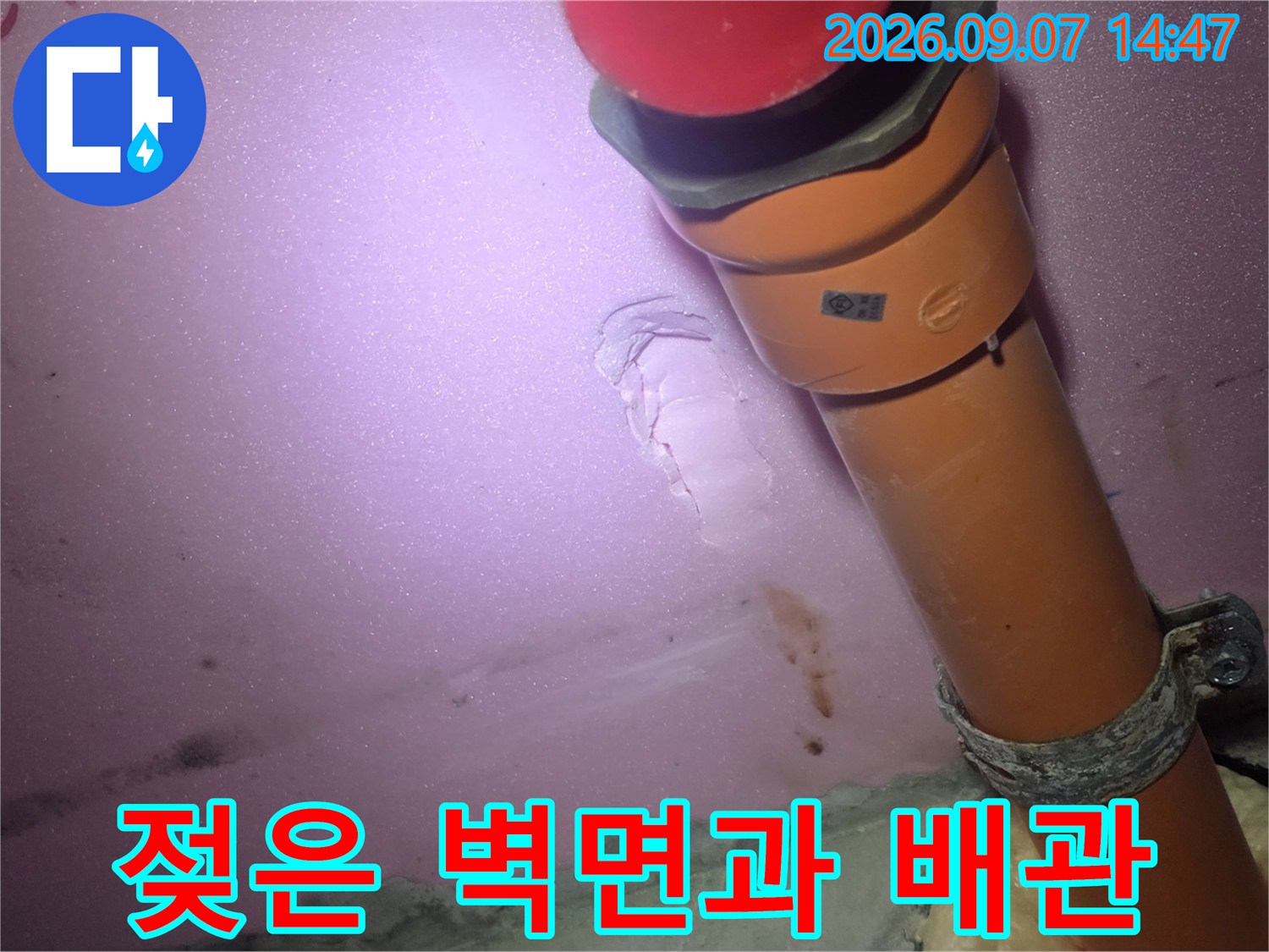 오렌지색 배관 하단부의 젖은 마감재와 누수 흔적 사진