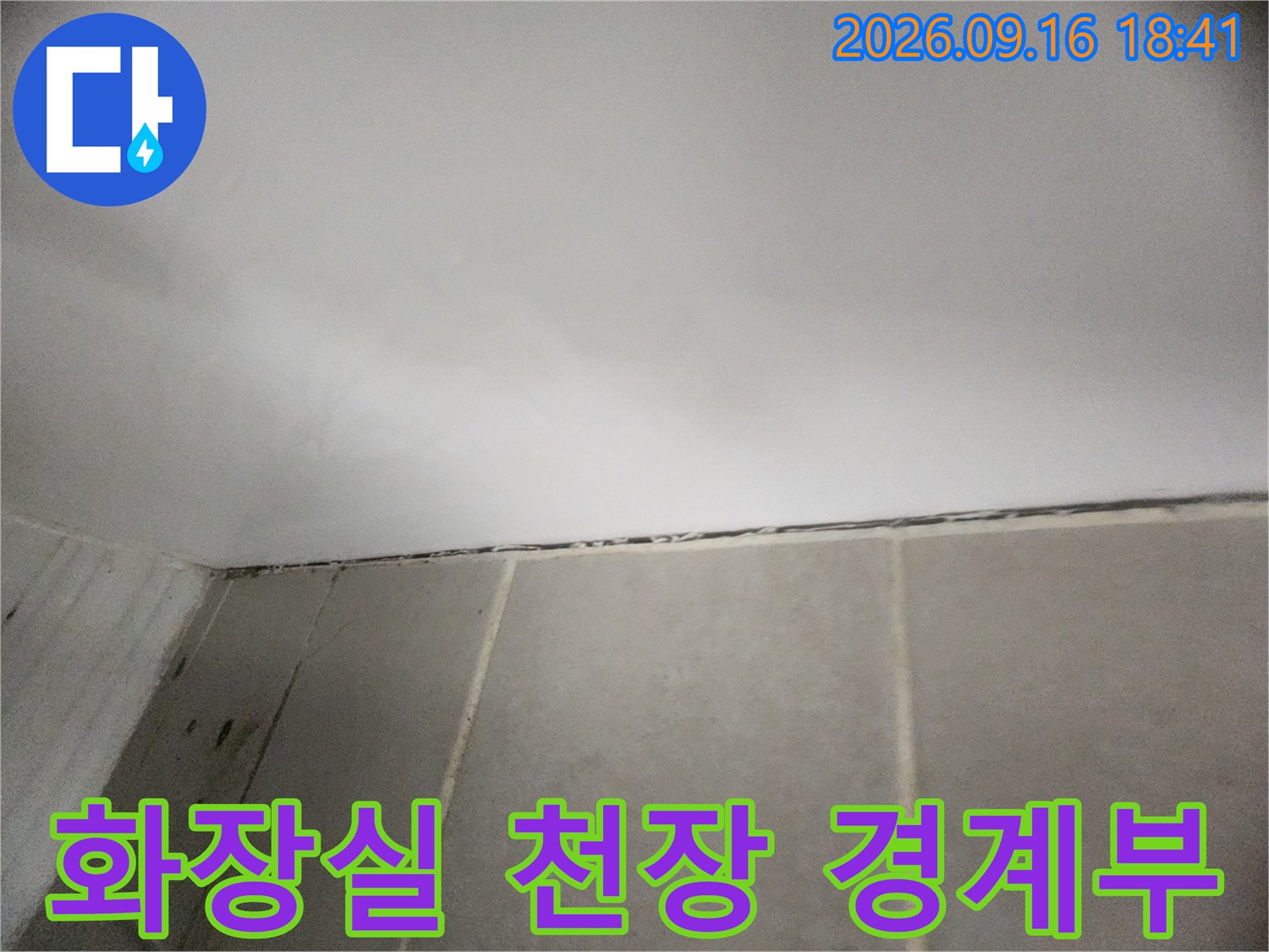 밝은 톤의 천장과 타일 벽면이 만나는 수평적인 접합 부위입니다.